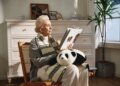 woman sits, reading, with a cuddly AI baby panda robot on her lap