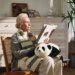 woman sits, reading, with a cuddly AI baby panda robot on her lap