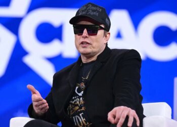 Elon Musk on stage at CPAC in Maryland with sunglasses on and a MAGA hat
