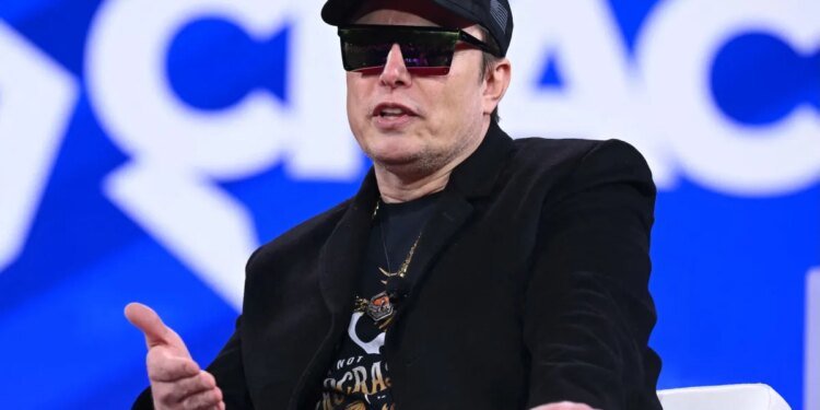 Elon Musk on stage at CPAC in Maryland with sunglasses on and a MAGA hat