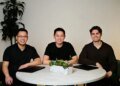 Three men in black shirts sit around a circular table
