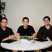 Three men in black shirts sit around a circular table