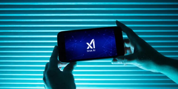 A person holds a telephone displaying the logo of Elon Musk s artificial intelligence grok in front of a background lit by a blue light.