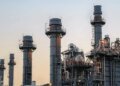 Natural gas power plant smoke stacks stand against a twilight sky.