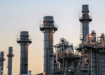 Natural gas power plant smoke stacks stand against a twilight sky.