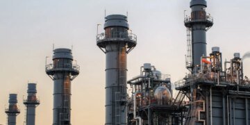 Natural gas power plant smoke stacks stand against a twilight sky.