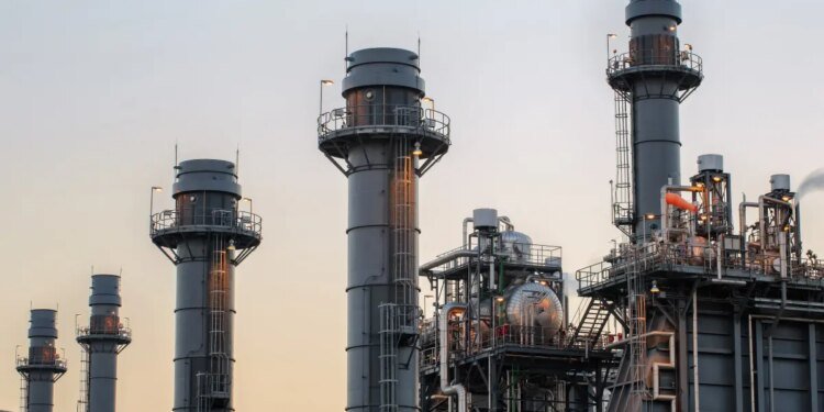 Natural gas power plant smoke stacks stand against a twilight sky.