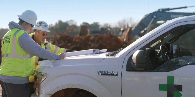 Two workmen look at plans on the hood of a Ford F150